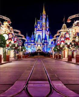 Cinderella Castle lit in blue at night with Christmas decorations and festive lights lining the street leading to it