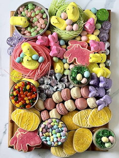 Easter dessert board with pastel cookies, macarons, candies, and chocolate eggs arranged on wooden platter
