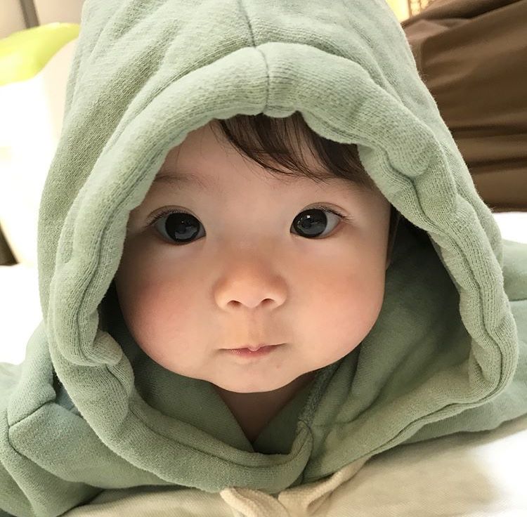 Baby with dark hair and eyes wearing a light green hooded towel, close-up portrait