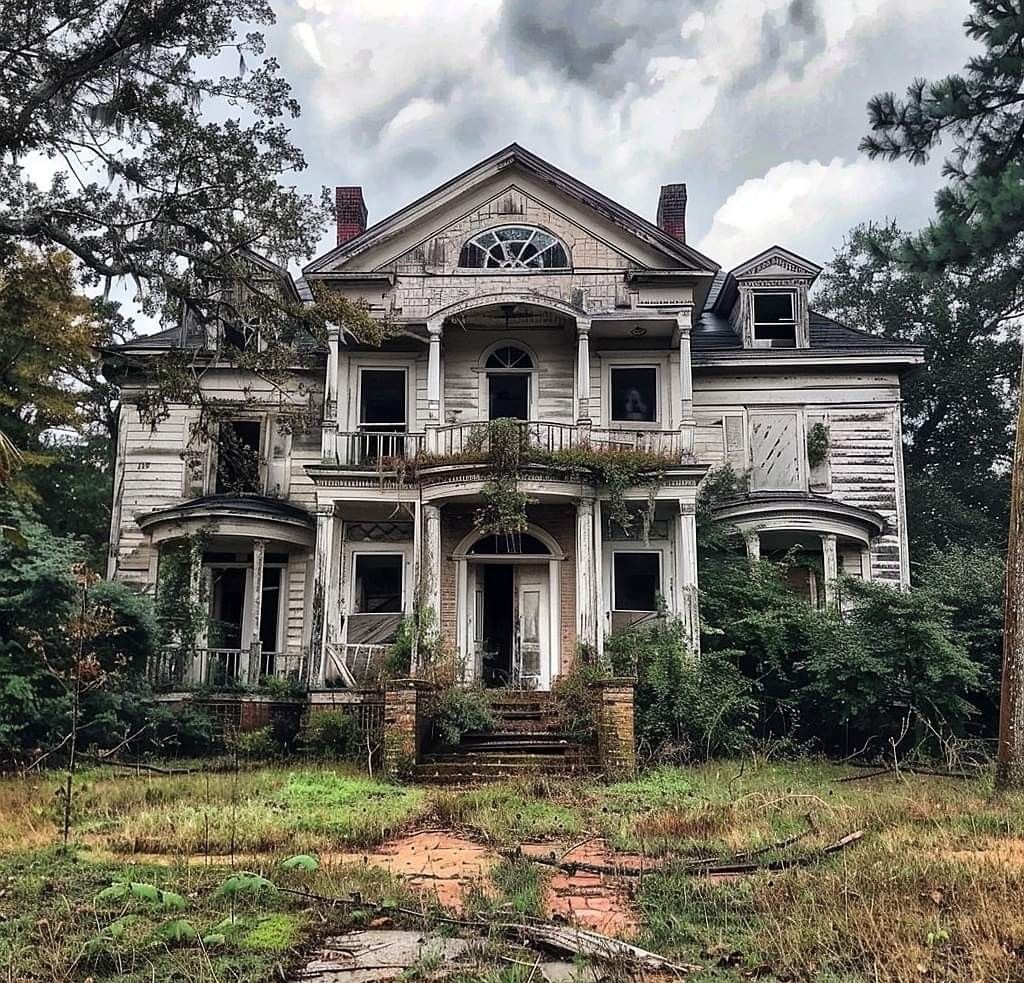 Abandoned Victorian house with broken windows and overgrown front yard under a cloudy sky