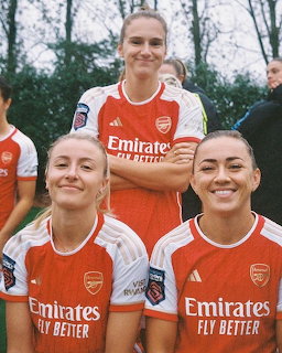 Three Arsenal women's football players in red and white kits posing together outdoors