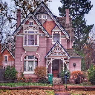 Pink Victorian house with decorative trim, front porch, and trees