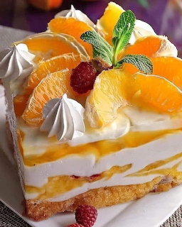 Slice of layered cake decorated with orange segments, whipped cream, raspberry, and mint leaf