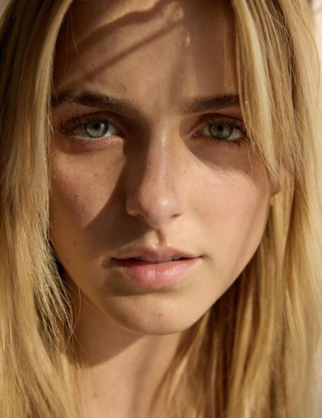 Close-up portrait of a young blonde woman with green eyes and freckles in natural light