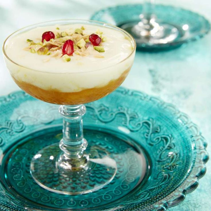 Layered cream dessert in stemmed glass topped with pistachios and pomegranate on turquoise decorative plate