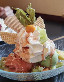 Tall ice cream sundae with wafers, cream, fruit and decorative leaf garnish on blue plate