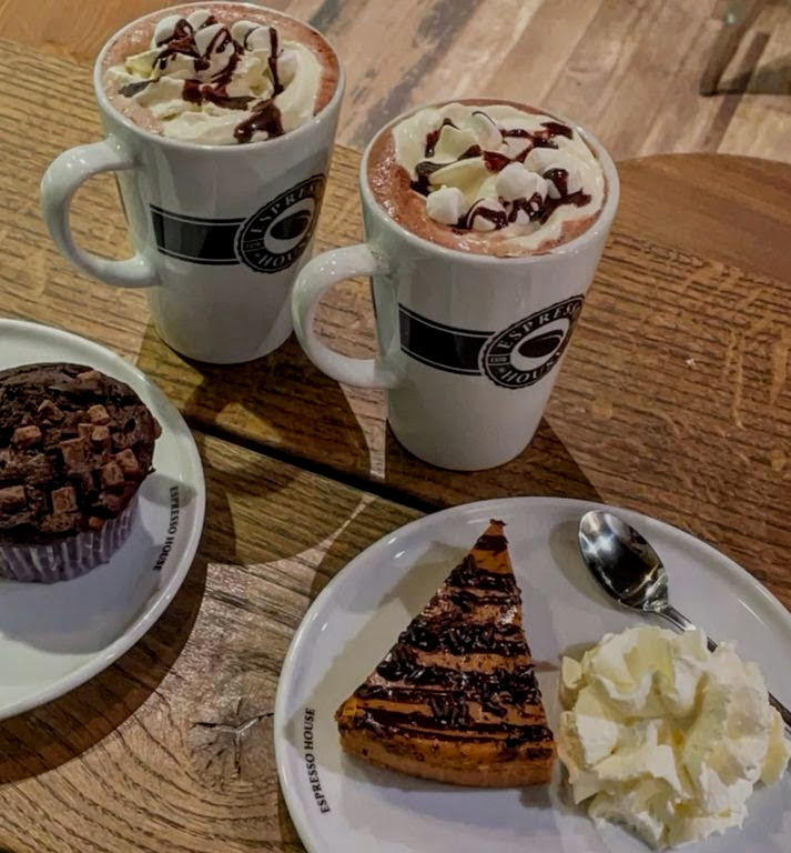 Two mugs of hot chocolate with whipped cream, chocolate muffin, and chocolate waffle with cream on wooden table