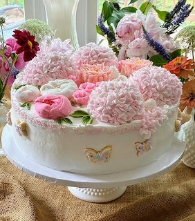 White cake decorated with pink carnations and roses on white pedestal stand with gold butterflies
