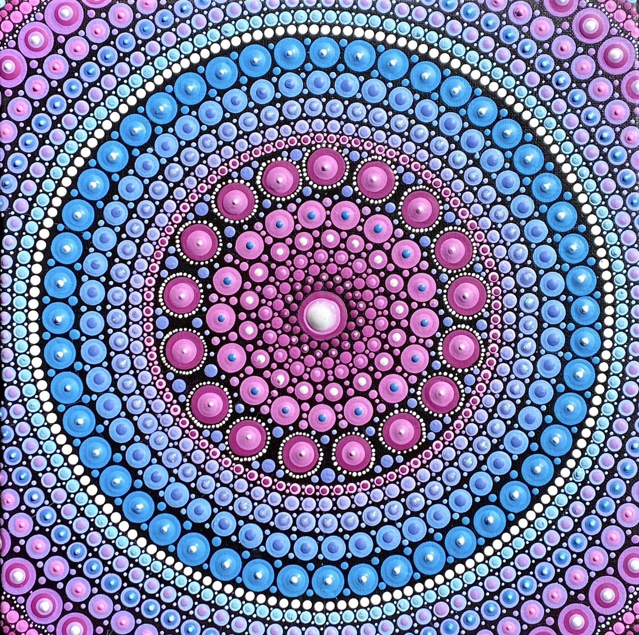 Circular mandala with concentric rings of pink, blue and white dots in symmetrical pattern