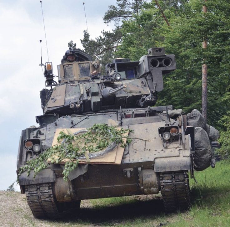 Front view of a Bradley military tank on grass beside trees