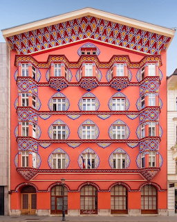 Symmetrical coral-pink building with ornate painted decorations and multiple arched windows
