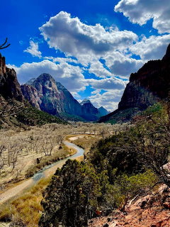 Scenic view of Zion National Park valley with sandstone mountains, winding river, and blue sky with clouds