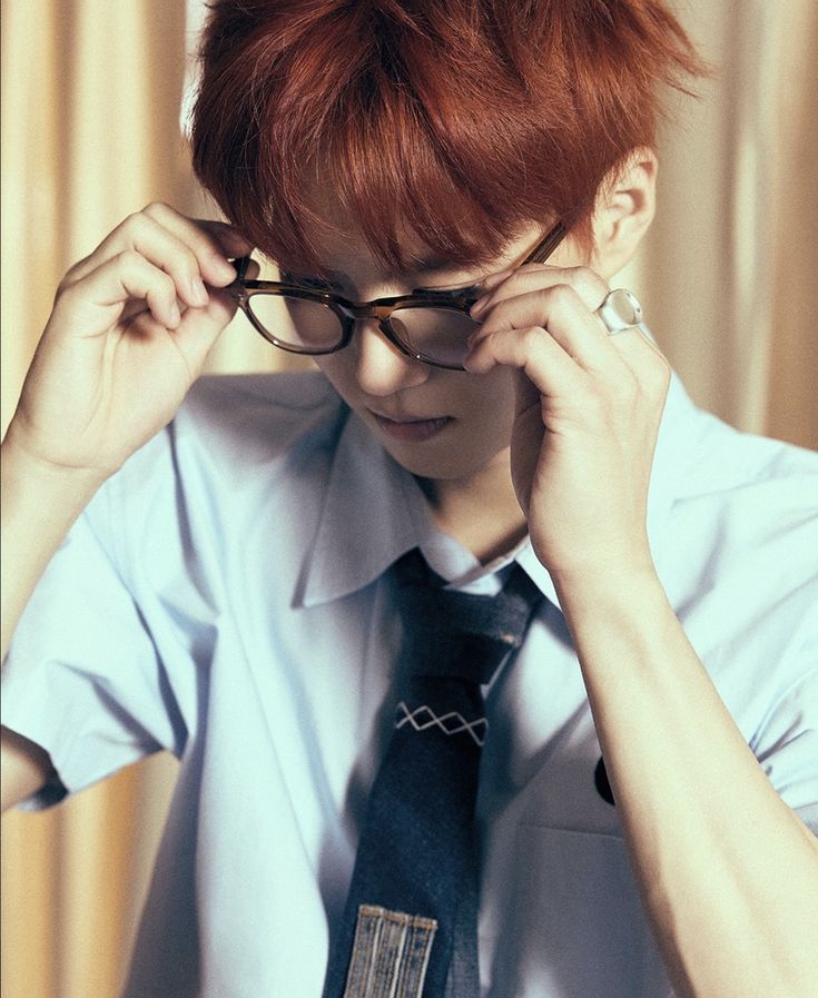 Young man with orange hair adjusting sunglasses, wearing white shirt and black tie