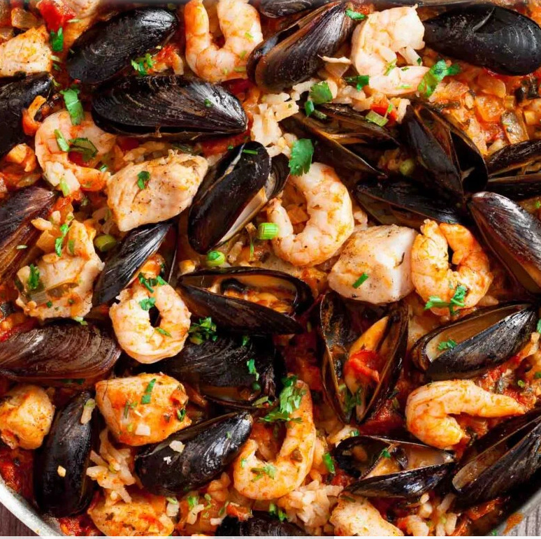 Overhead view of seafood paella with mussels, shrimp, rice, and chopped green herbs