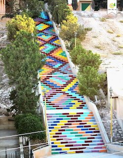 Outdoor staircase painted in bright geometric colors, rising uphill between trees