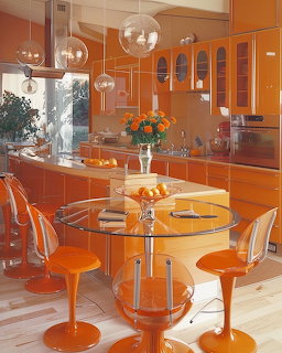 Bright orange1970s retro kitchen with tulip chairs, glass table, globe pendant lights, and orange flowers