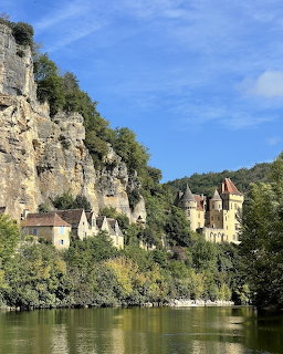 Medieval château at the base of tall limestone cliffs beside a calm river with green reflections