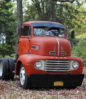 Vintage orange 1942 Ford COE truck with chrome grille parked outdoors in autumn setting
