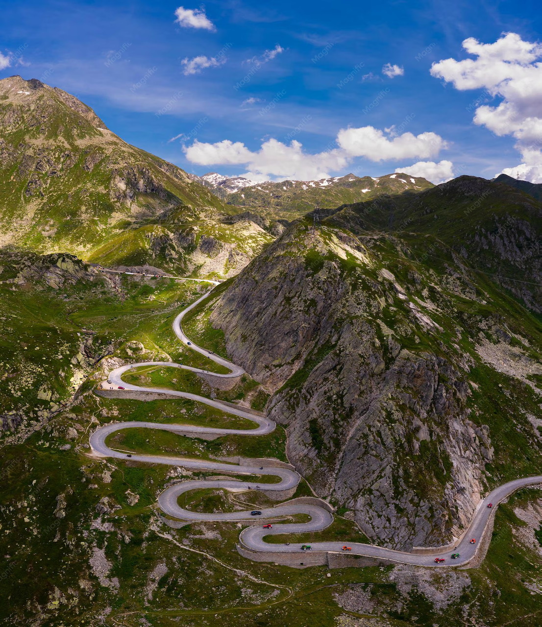 Aerial view of serpentine mountain road with multiple hairpin turns through rocky alpine landscape