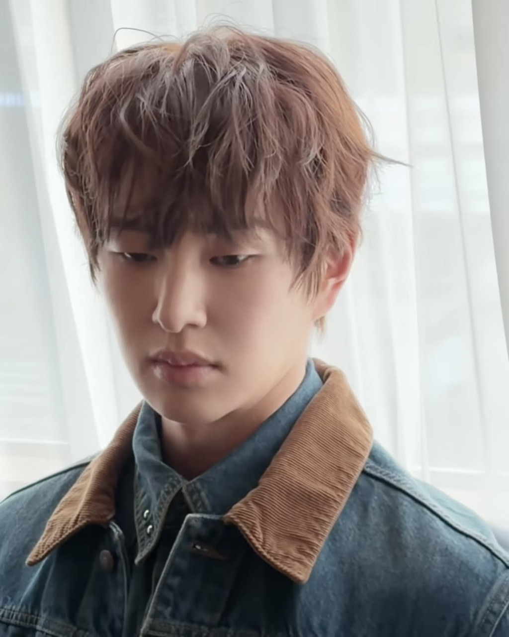 Portrait of young man with brown hair in denim jacket looking at camera