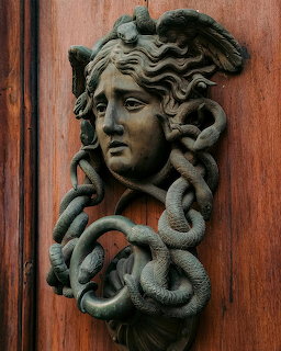 Bronze Medusa head door knocker with snake hair on a wooden door