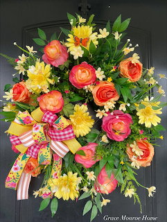 Colorful floral wreath with pink roses, yellow daisies, and checkered ribbon on dark door
