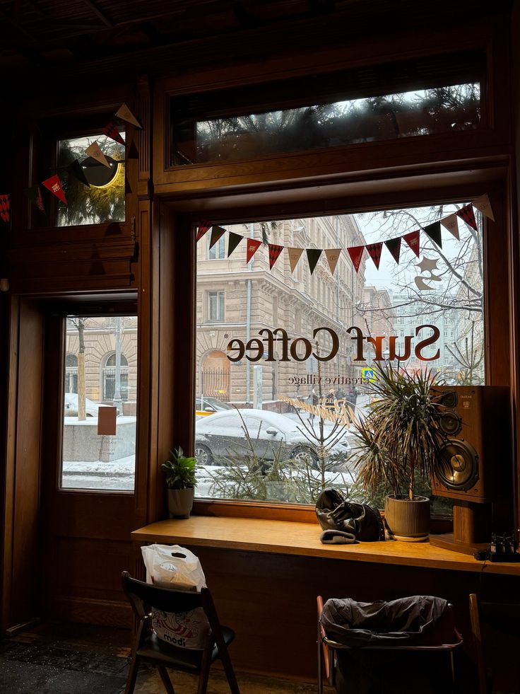 Cozy cafe interior with 'Surf Coffee' window lettering, bunting flags, wooden counter, and snowy street outside