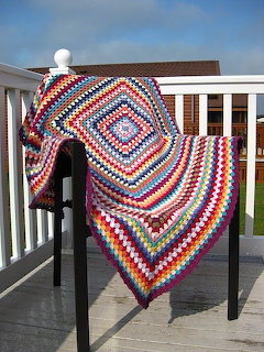 Colorful crochet granny square blanket draped over a white balcony railing outdoors