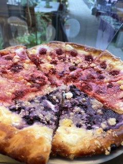 Sliced round fruit cake with berry and crumble toppings on a plate near a window