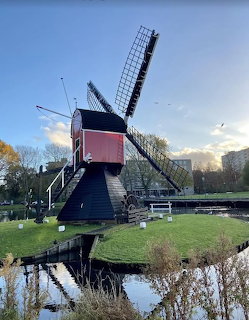 Traditional windmill beside a canal and grassy bank under a blue sky
