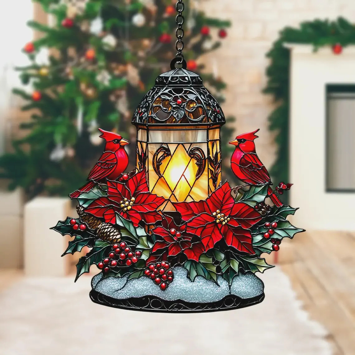 Ornate suncatcher with cardinal birds, poinsettias and illuminated lantern on table before Christmas tree