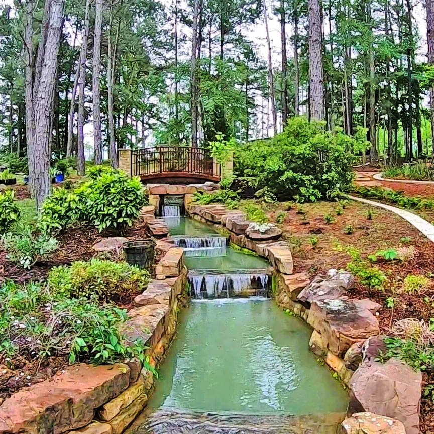 Stepped waterfall stream flowing through landscaped park garden with pine trees and walking paths