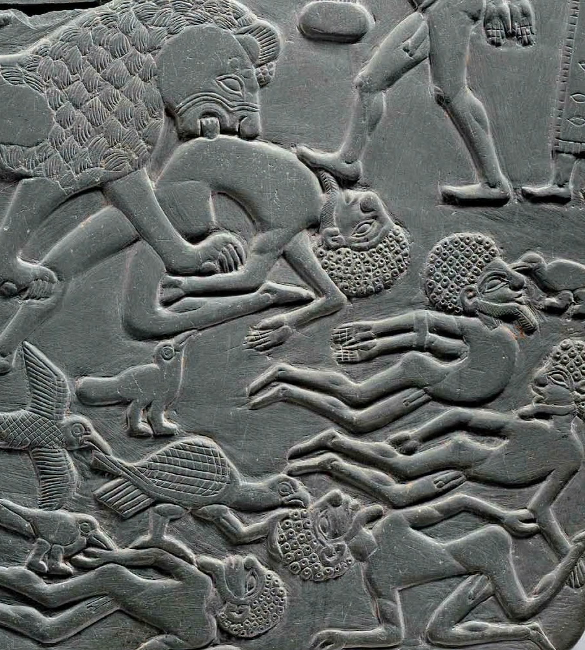 Ancient gray stone relief carved with warriors, fallen figures, animals, and weapons in battle.
