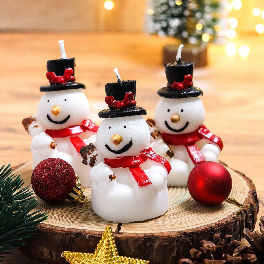 Three decorative snowman candles with top hats and red scarves on wooden base with Christmas ornaments