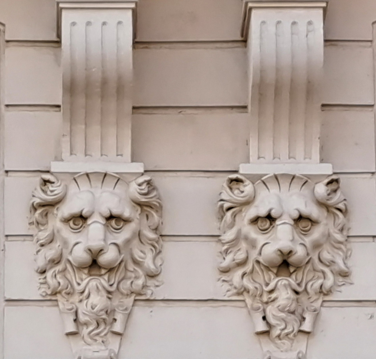 Two carved lion head mascarons on a pale stone facade
