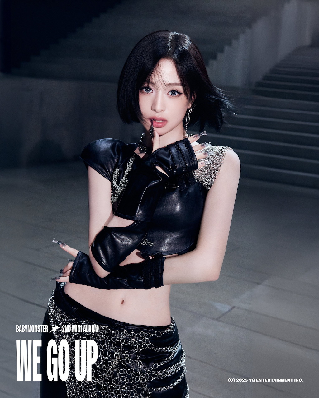 K-pop artist in black leather crop top and sequined skirt posing with dramatic lighting, WE GO UP text visible