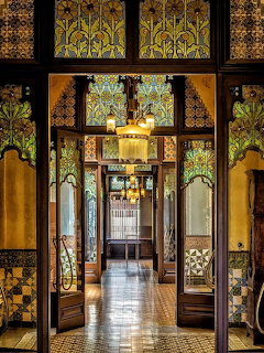 Ornate Art Nouveau hallway with stained glass, wooden doors, mosaic floors, and chandelier