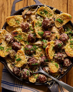 Cast iron skillet with roasted potatoes and meatballs garnished with parsley on wooden surface