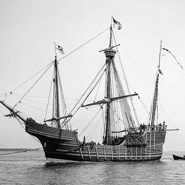 Historic three-masted wooden sailing ship in black and white photograph on calm water