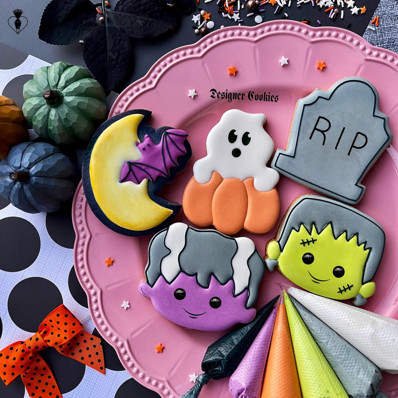 Assortment of decorated Halloween cookies on pink plate with spooky designs including ghost, pumpkin, and tombstone