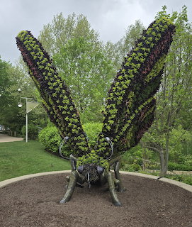 Large butterfly-shaped plant sculpture with green and purple foliage wings in a park