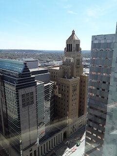 Tall historic clock tower with dome rising among modern glass and concrete buildings in city skyline
