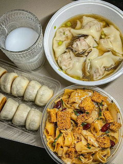 Overhead view of Korean meal with soup, dumplings, rice rolls, spicy stir-fried vegetables, and water
