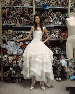 Woman in a white bridal gown standing before shelves of rolled fabric