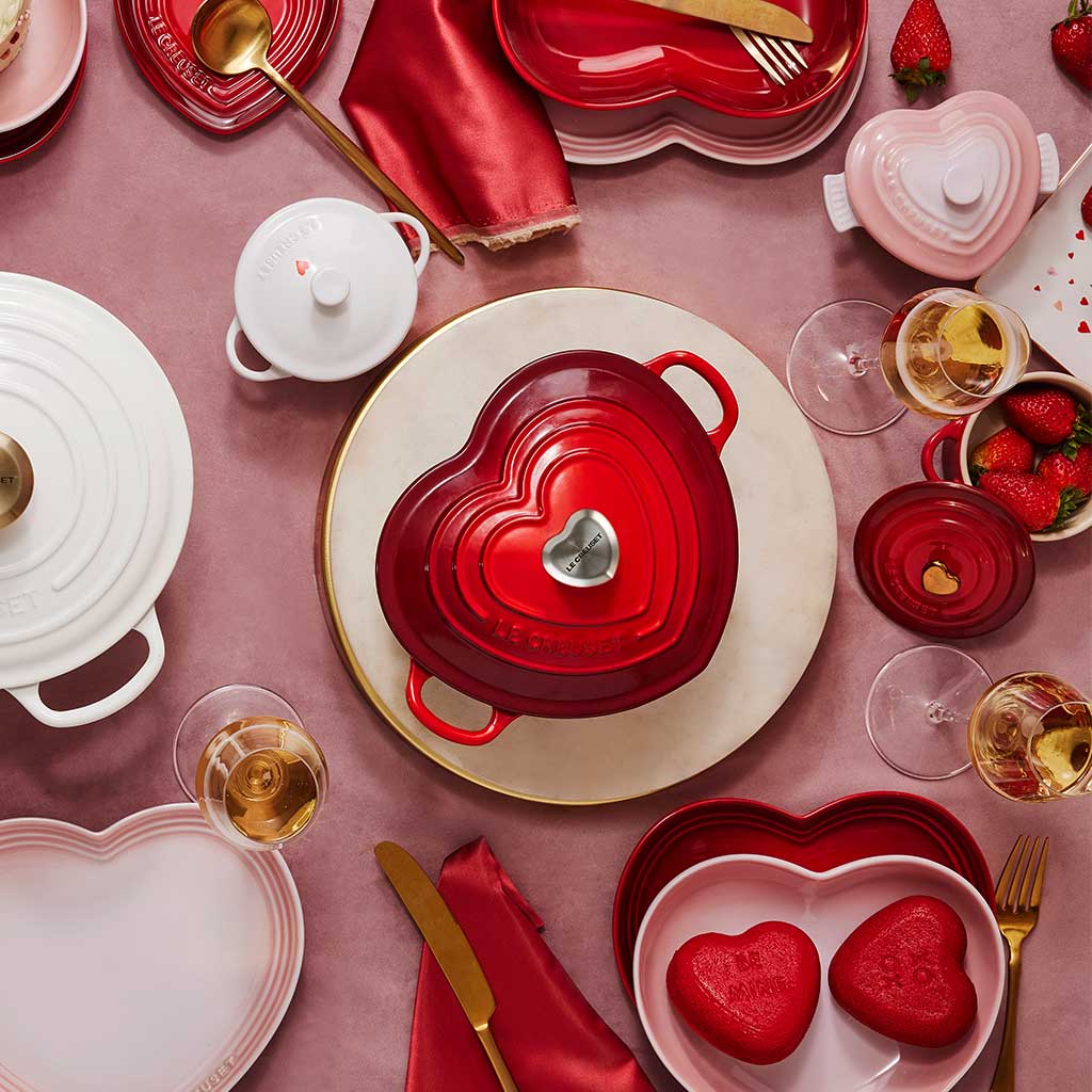 Red and pink heart-shaped pots, dishes and kitchen items on pink background