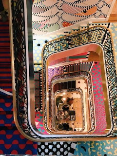 Top-down view into a colorful multistory stairwell with patterned carpets and decorative railings.