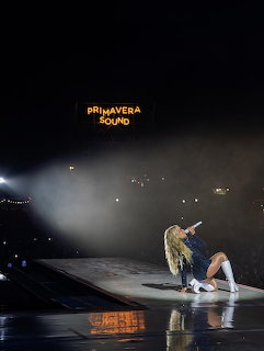 Blonde female singer crouching on stage at Primavera Sound concert holding a microphone
