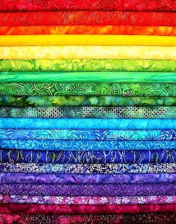 Stack of colorful fabric rolls arranged in rainbow order with decorative patterns