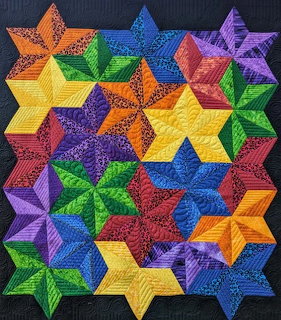 Colorful quilt with overlapping six-pointed stars in rainbow hues creating geometric pattern on dark fabric background