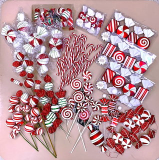 Red and white peppermint Christmas ornaments and candy canes arranged in circular wreath pattern on pink background